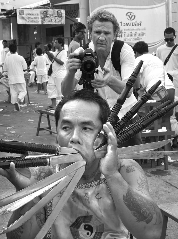 Man taking picture of a man with a lot of knives in his mouth