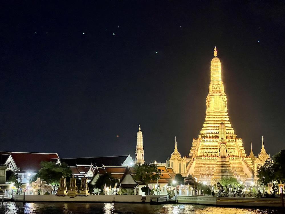 Lighted tower near other building and body of water during night time