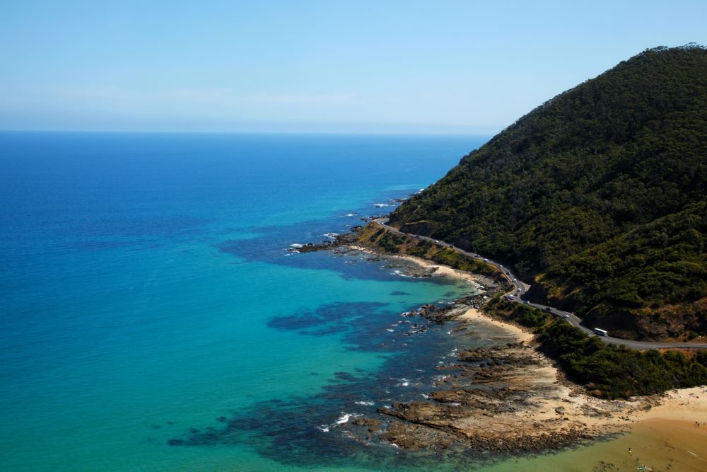 aerial view of a road in between lushy green mountain and the ocean - Best Beaches in Australia