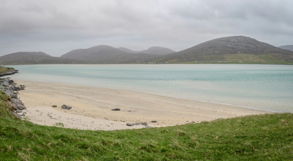 white sand beach surrounded by green grass and mountain