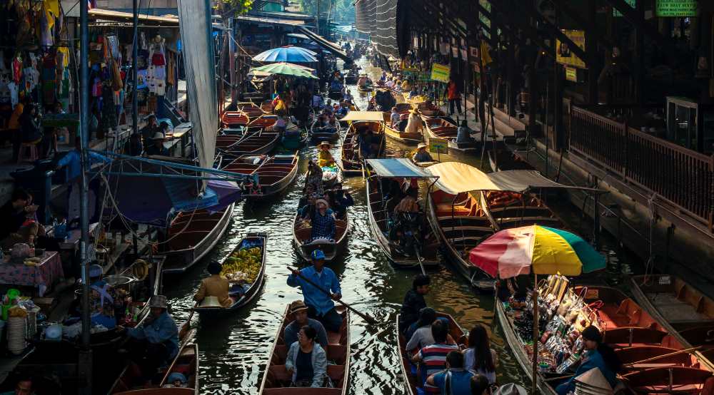 boat full of different veggies, fruits and other things to sell in a body of water with a lot of people