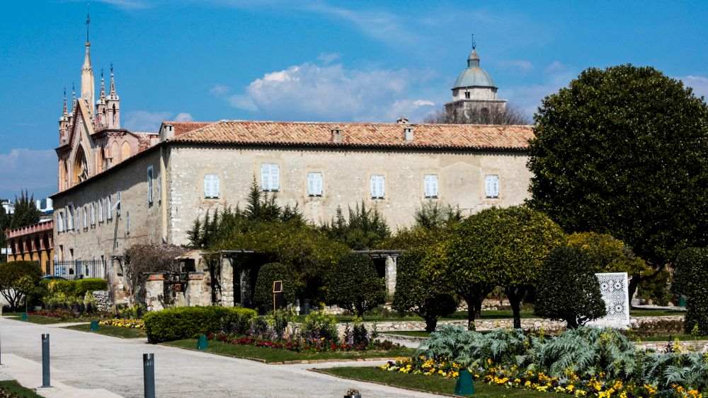 old stone building surrounded by colorful flowers and green plants and trees