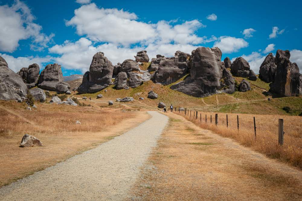 dirt road in the field with huge rock in the background