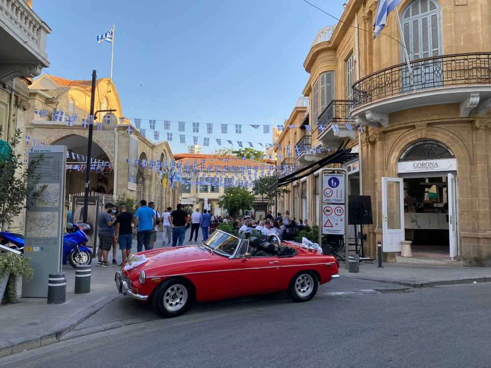 red car park in front of a street with people walking- cyprus digital nomad visa