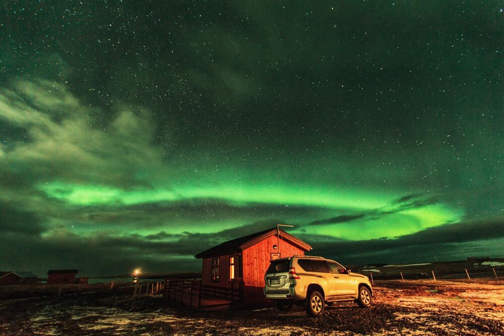 Northern Lights Iceland with small red barn house and SUV