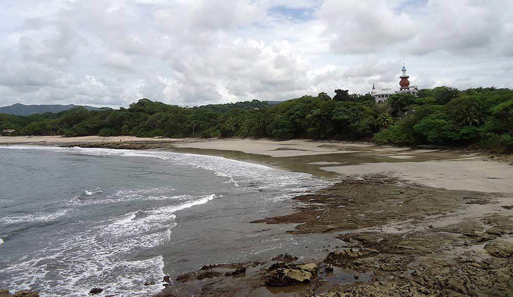 side view of Nosara Beach, Nicoya Peninsula with forest beside and a white house with steeple tower in the middle