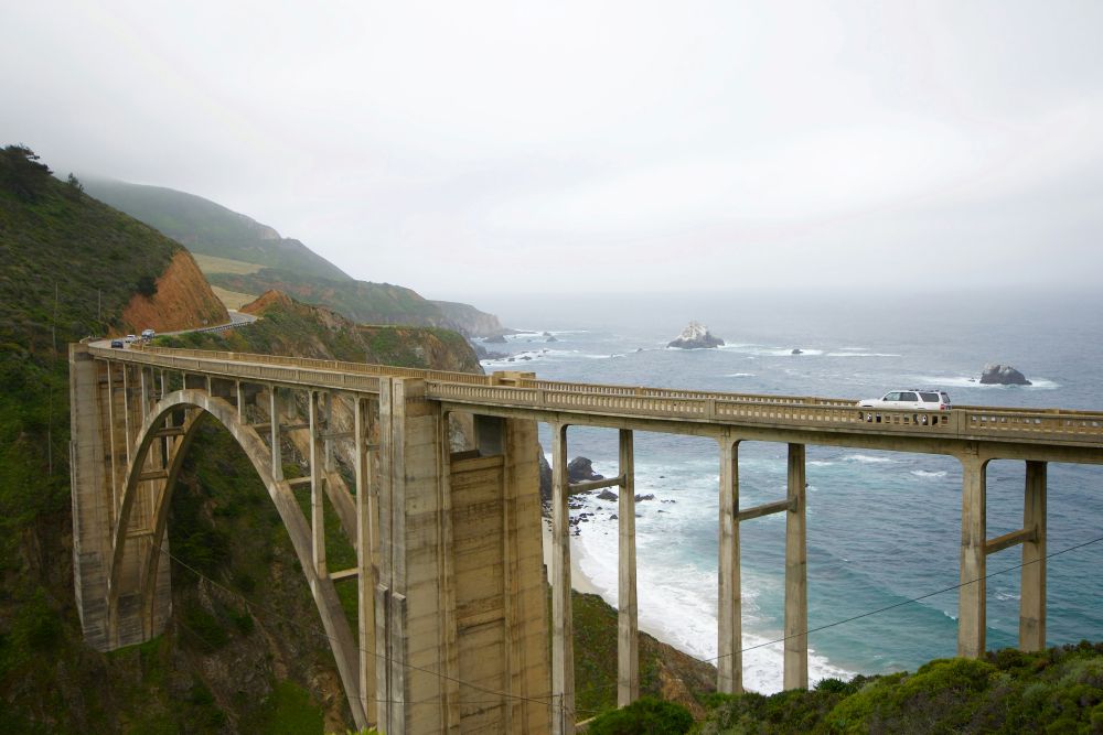 car driving at the bridge over the ocean and mountains - Best road trips in the world