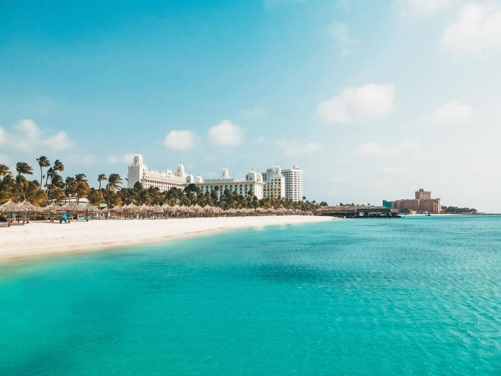 calm blueish beach and wite sand with huge white building at Palm Beach Aruba