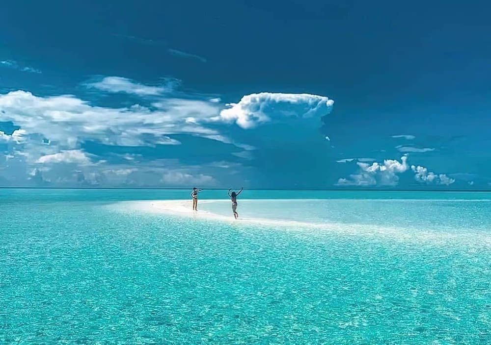 two people in the thin white sand in the middle of the clear blue beach