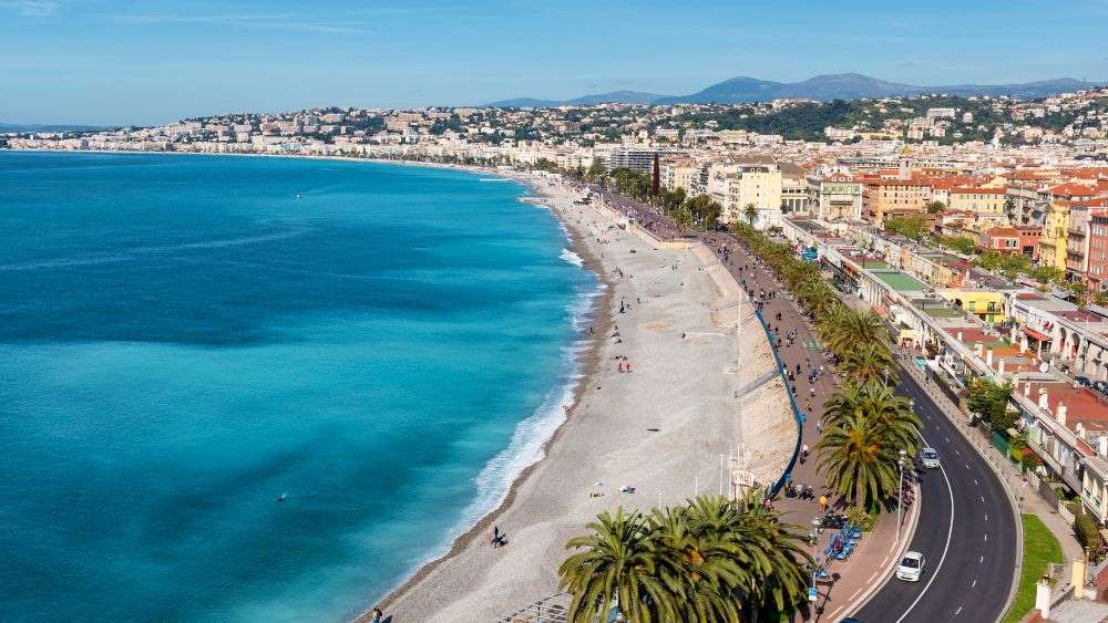 aerial view of a coastal walkway, one side is the body of water and the other side is the city full of houses and buildings - Things to do in Nice, France