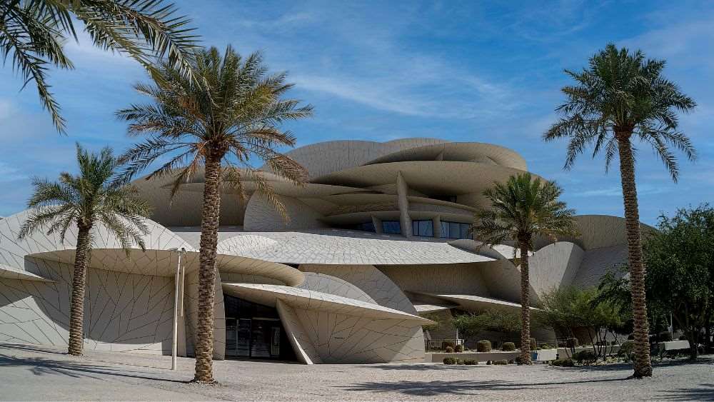 odd shape off white building surrounded by palm trees