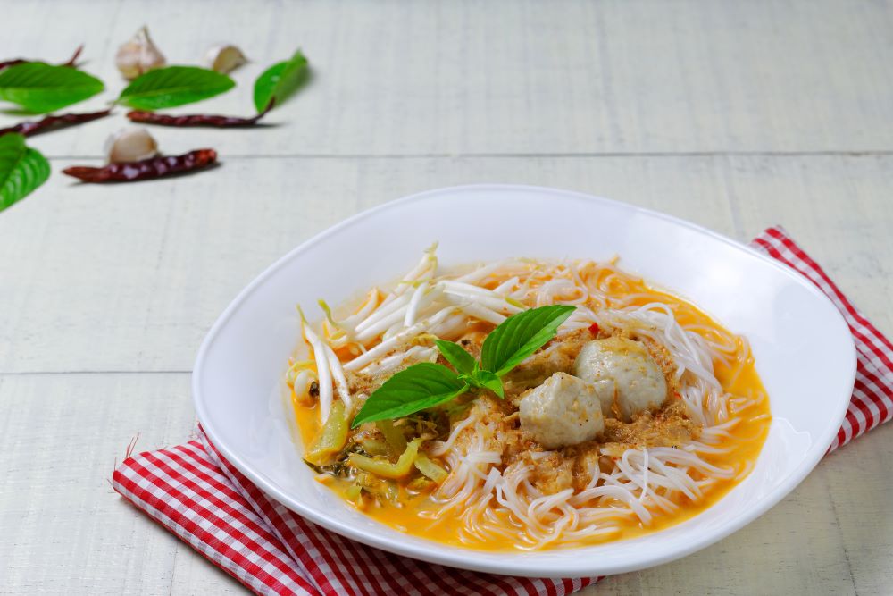Rice noodles in fish curry sauce top with small green leaves