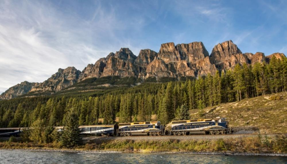 yellow blue train near travelling in between body of water and mountain - most beautiful train rides in the world