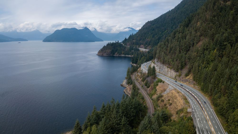 aerial view of a long highway road near in between mountain and ocean- Best road trips in the world