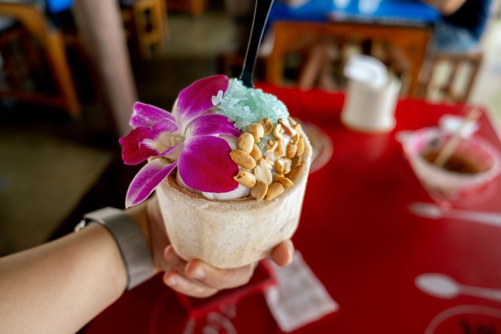 ice cream in coconut shell top with a purple flower and nuts