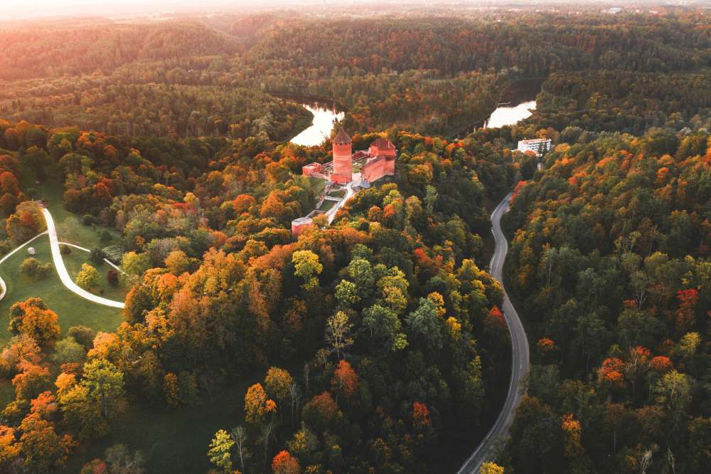 aerial view of a castle like building in the middle of the hill surrounded by green trees- latvia digital nomad visa