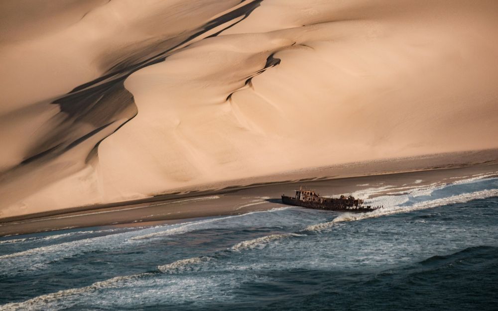 sand near body of water with shipwreck in it