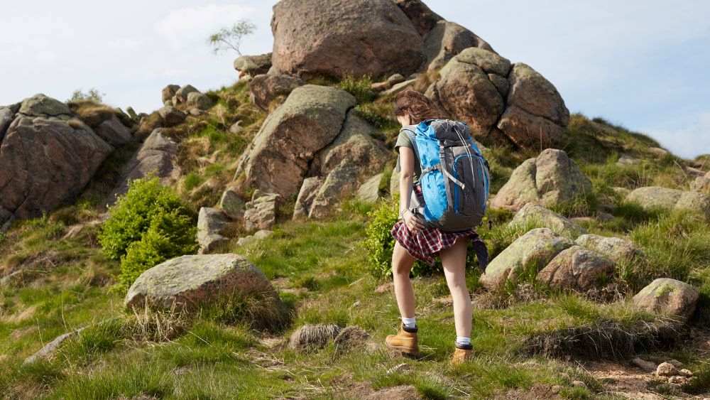 woman with back pack going in top of a hill with rocks