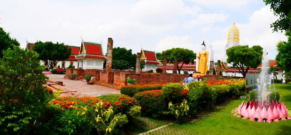 fountain in the side of the park with flowers and plants and beside a standing statue.