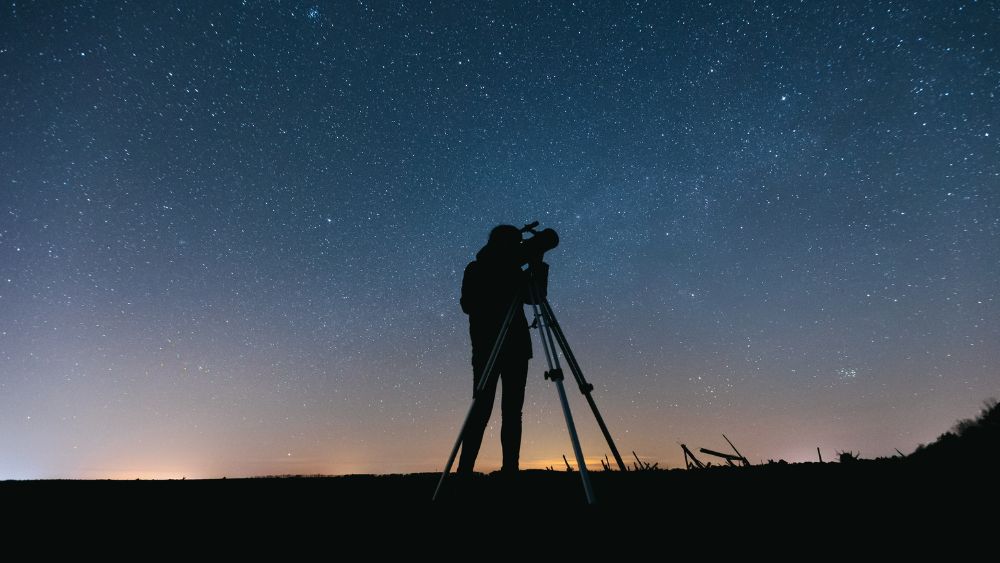 standing in front of the telescope looking at the sky full of stars