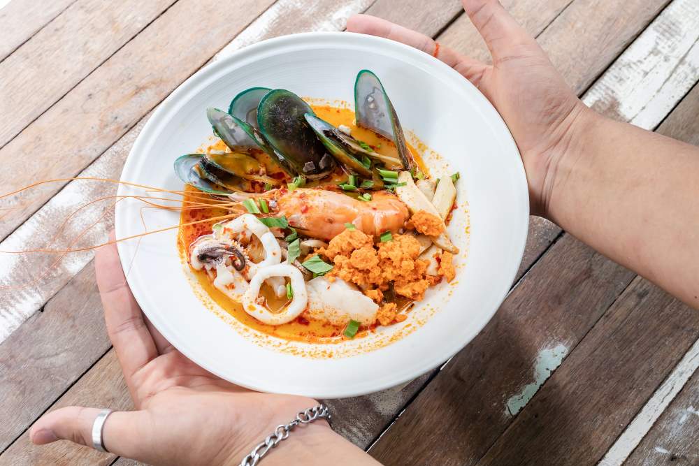 mix mussels shrimp and squid in a orange soup in a white plate - best thai food in thailand