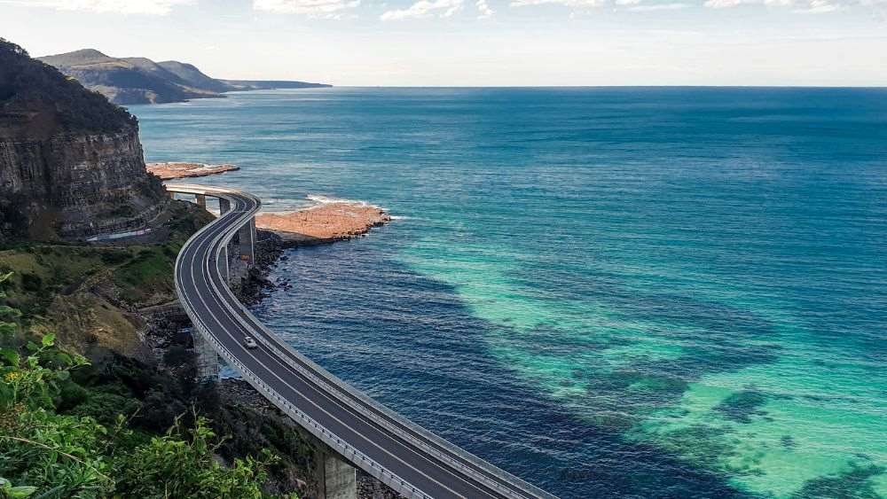 aerial view of a car strolling at an empty road near the coast - Exploring the Sydney to Melbourne Coastal Road Trip