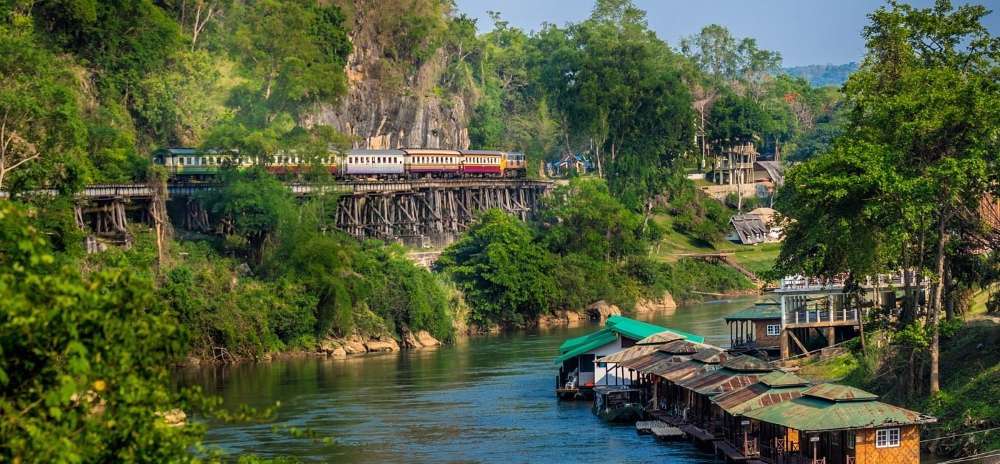 colorful train at the edge of the picture near the mountain surrounded by trees and beside body of water