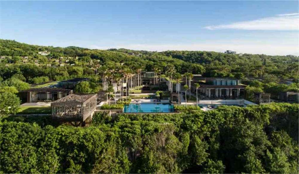 aerial view of a hotel building with swimming pool surrounded by green trees