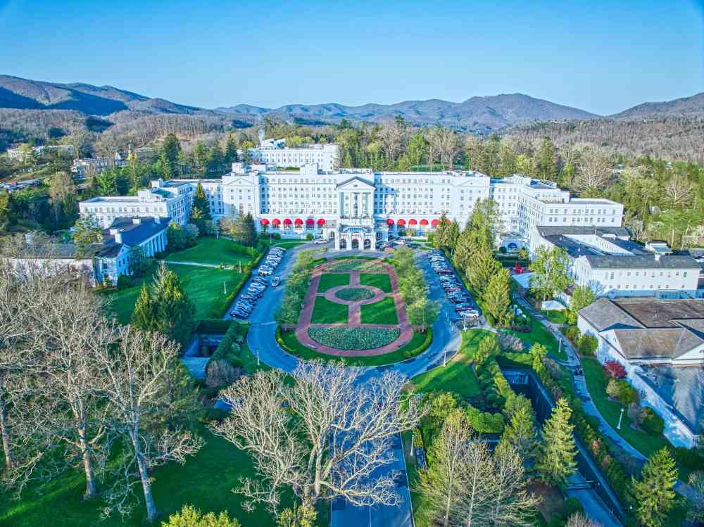 aerial view of a wide white building hotel surrounded by trees - unique hotels in the world