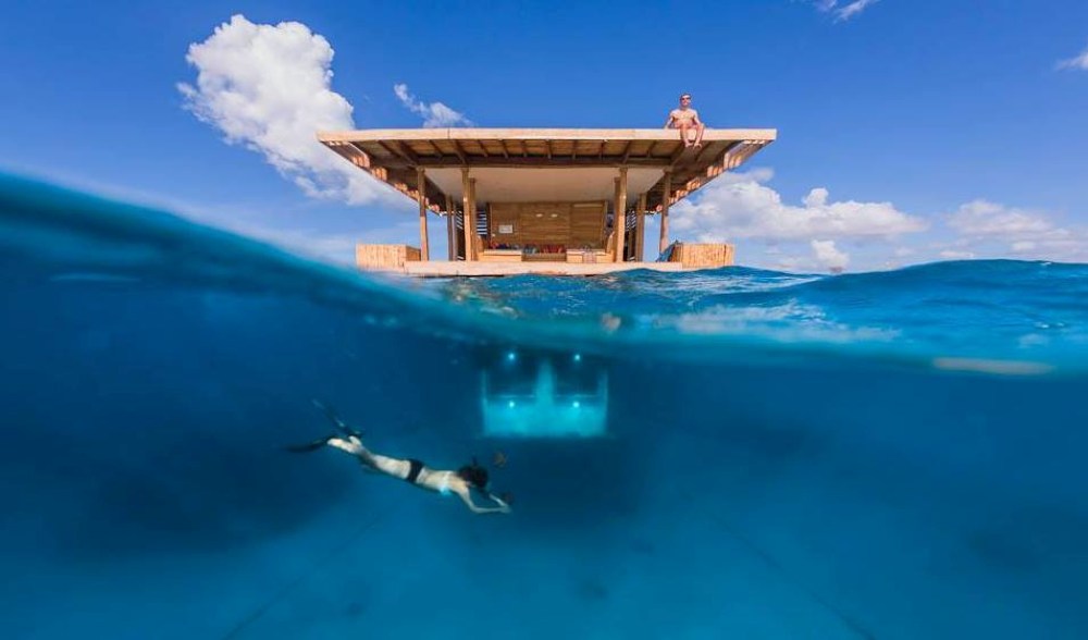 woman diving near a private room in the middle of the ocean with man on the roof - unique hotels in the world