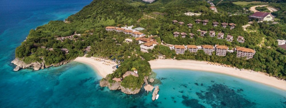 aerial view of a hotel buildings in an island surrounded by trees and near ocean