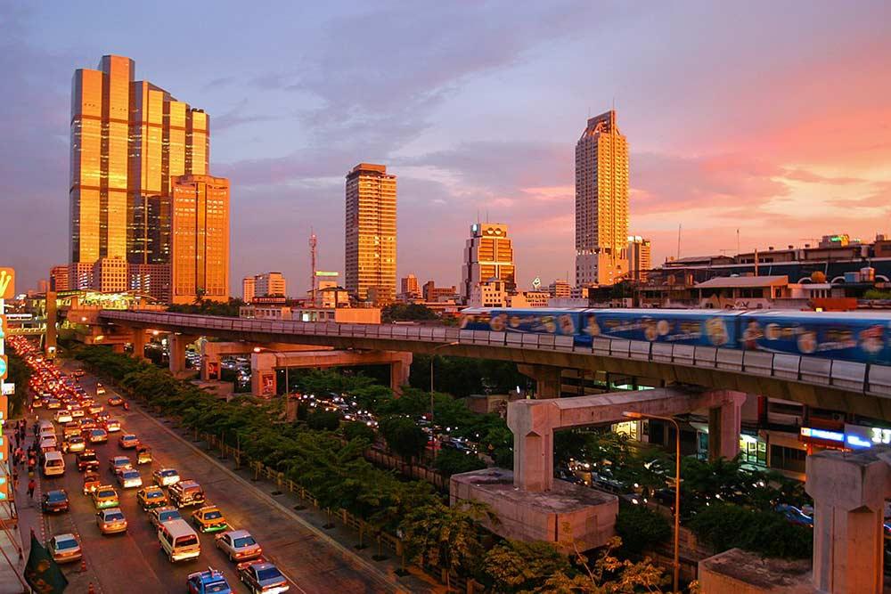 tall buildings and a lot of vehicles on the road under and above is a train at sky train during sunset