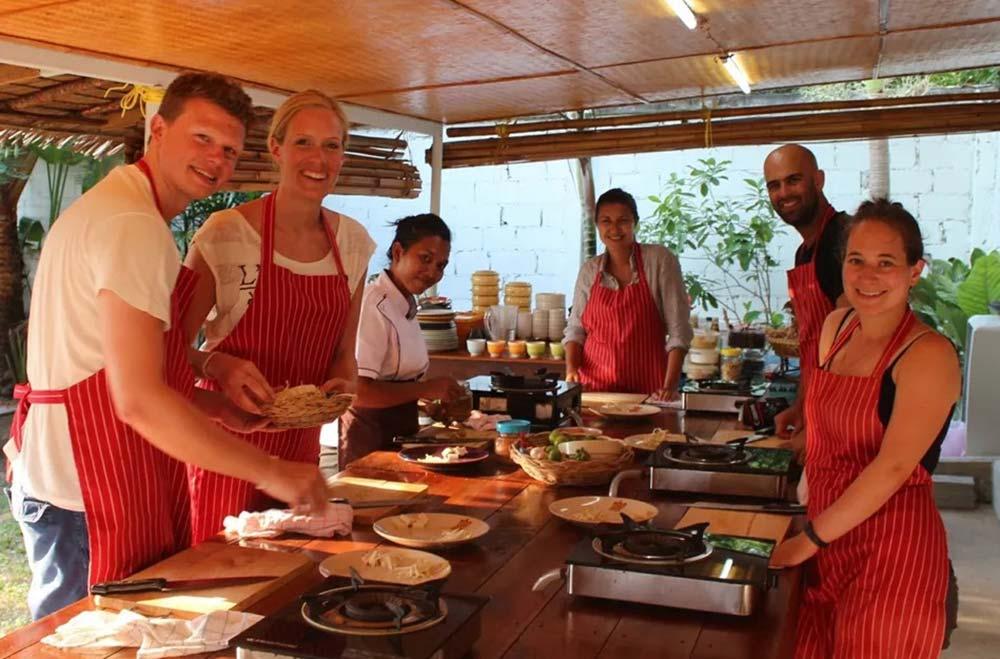 People posing for picture wearing red apron who are cooking