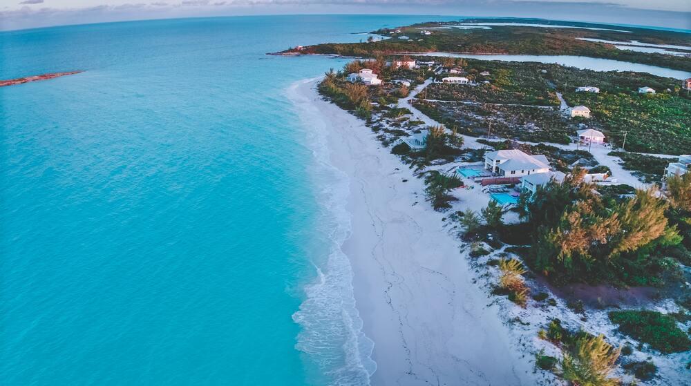 Aerial view of a beautiful blue sea white sand and a white house surrounded by gr5een trees in Tropic of Cancer Beach 