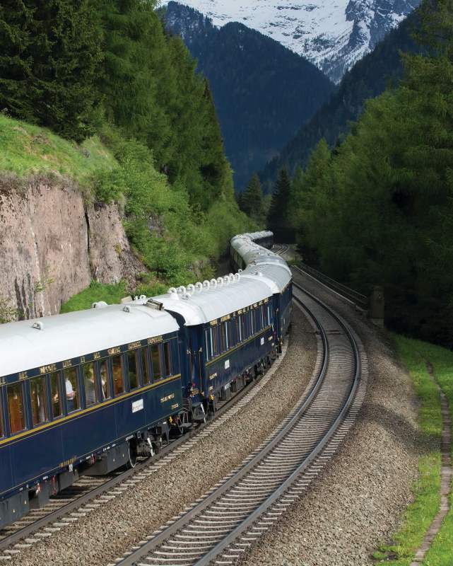 Navy blue train passing by lushy green forest - most beautiful train rides in the world