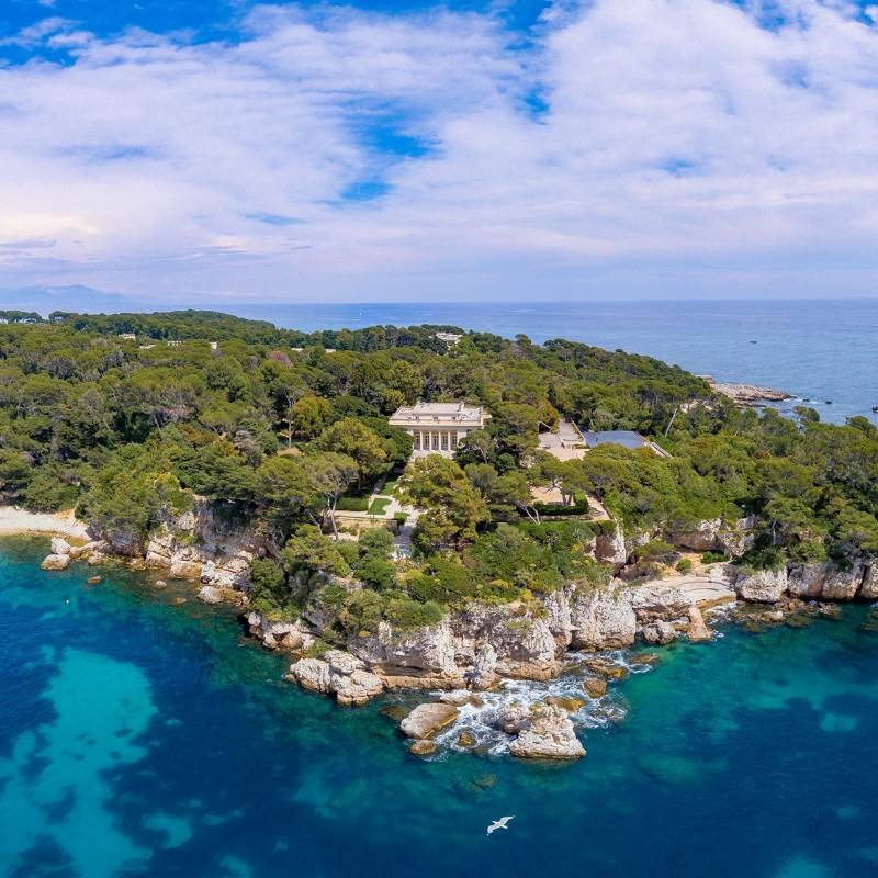 aerial view of an island surrounded by green trees with white building in the middle - Best Things to Do in Antibes