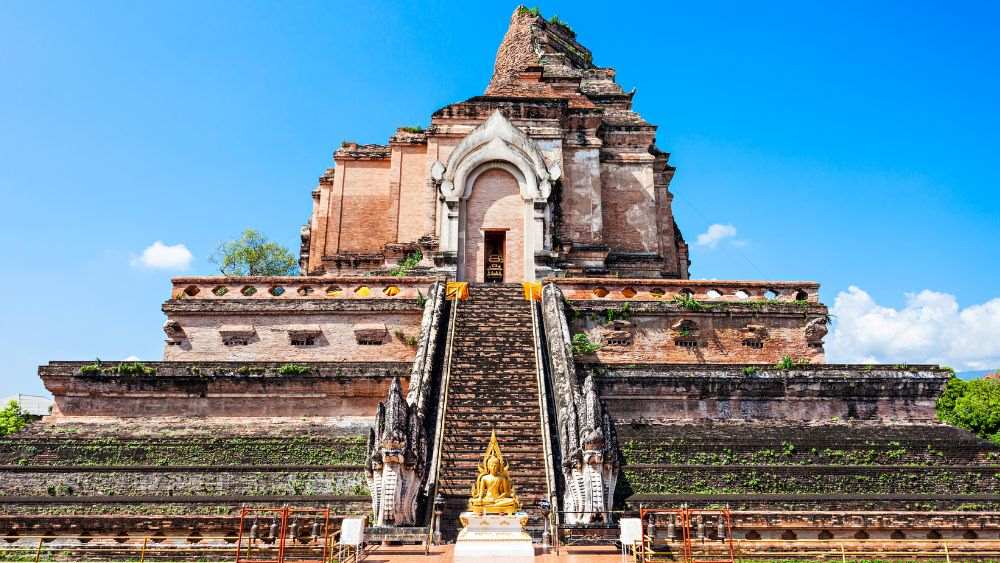golden buddha in the middle with stairs going to a brown concrete structure- things to do in chiang mai