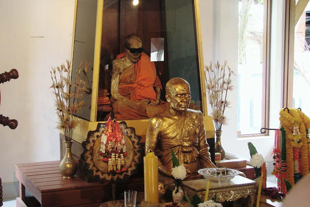 a mummified monk displayed in a glass case and golden statue in front of it