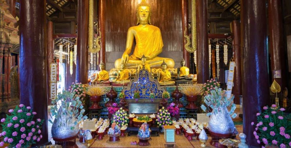 one big golden buddha statues surrounded by small buddha and with flowers- chiang mai temples