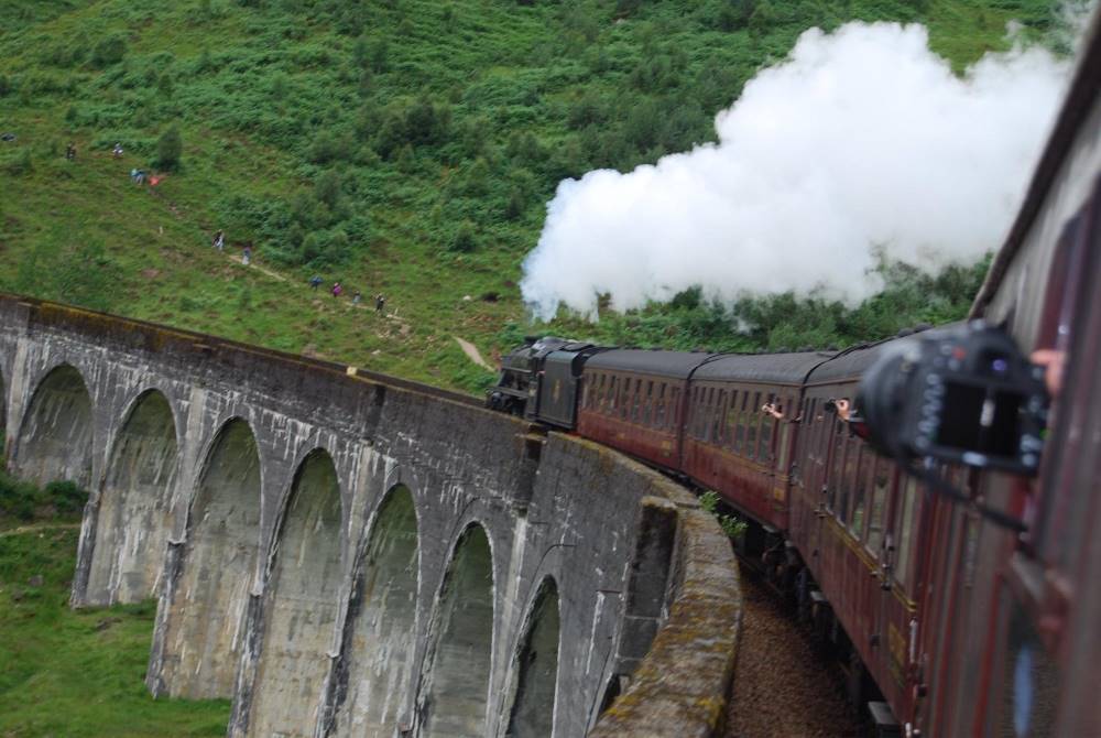 train showing smoke passing by green hill - most beautiful train rides in the world