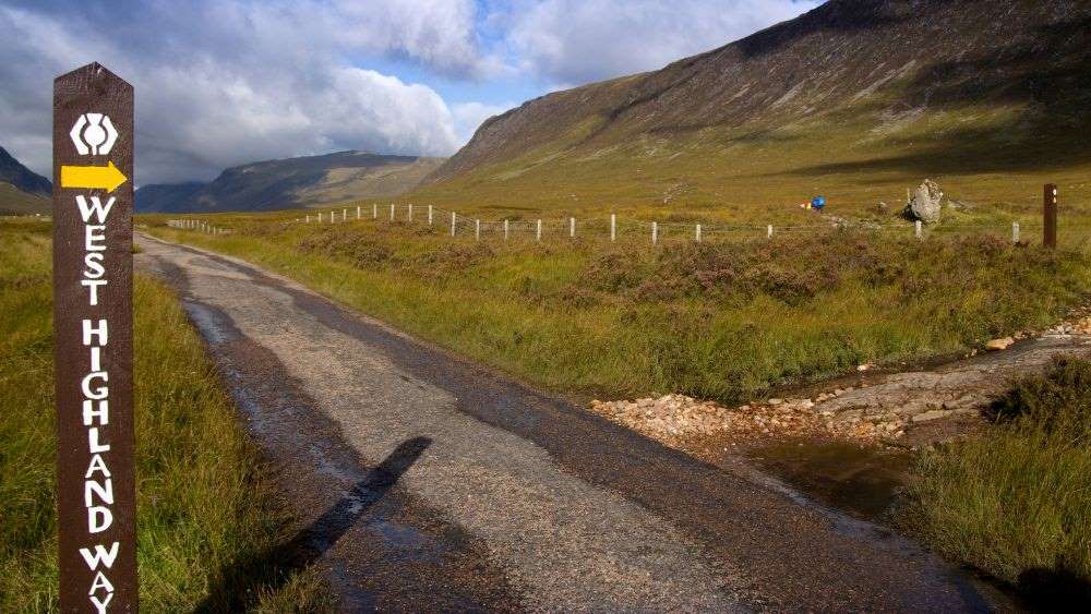 sing at the beginning of the road surrounded by mountain and green grass- Things to Do in Scotland