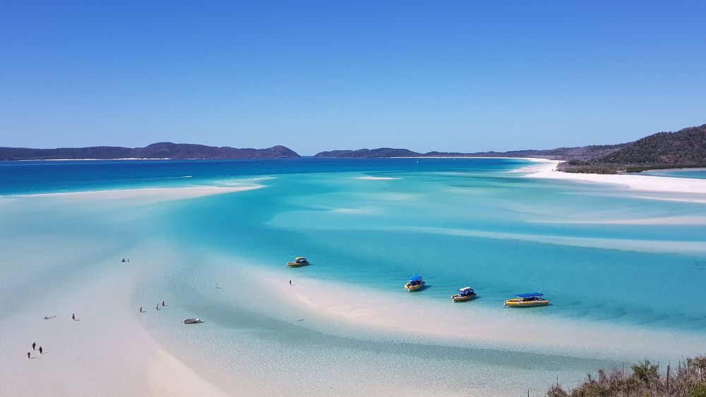 boats at the edge of the ocean near the white sand