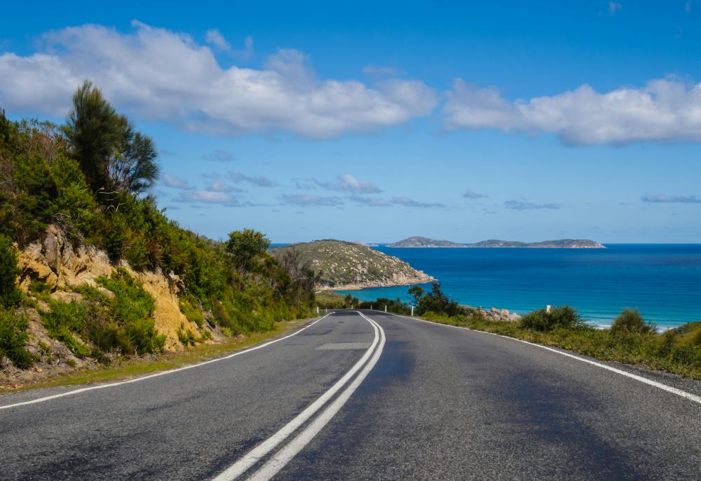 road with blue ocean on the right and rocky mountain on the left side - Exploring the Sydney to Melbourne Coastal Road Trip