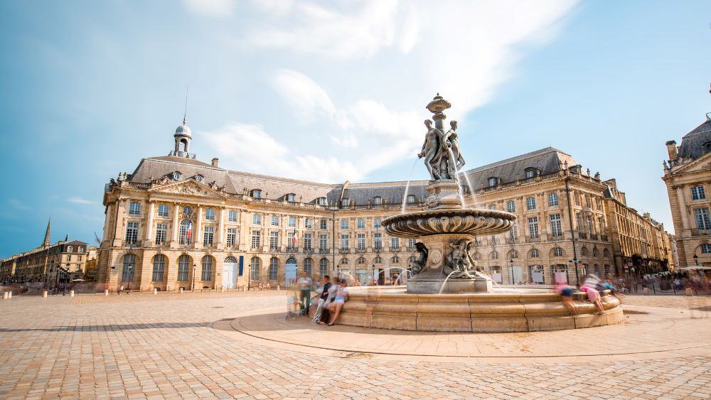 people sitting at a fountain in the middle of an open place with old structure building at the back - Oldest Cities in Europe to Visit in 2025
