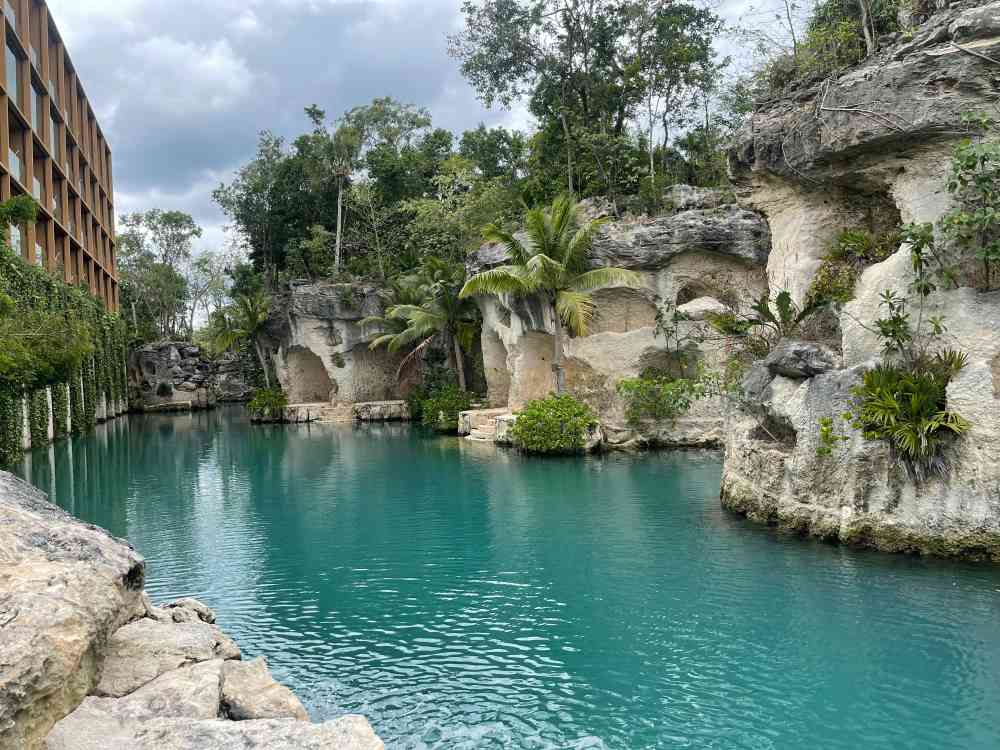 large body of water surrounded by cave-like stone with green trees