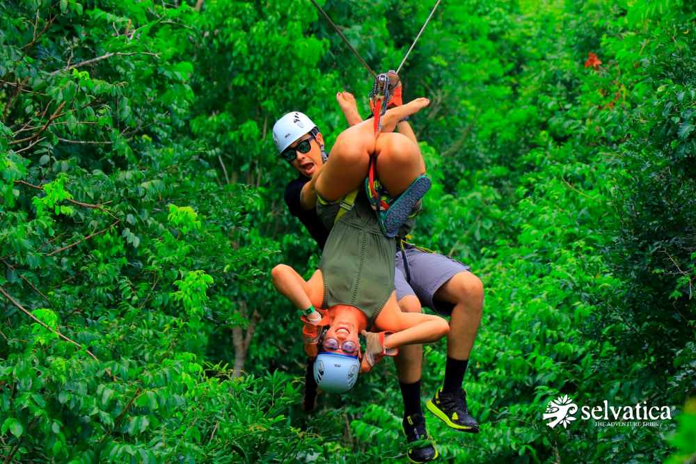 man and woman doing zip line in the middle of the forest, the woman is upside down- Best Things to Do in Cancun Mexico